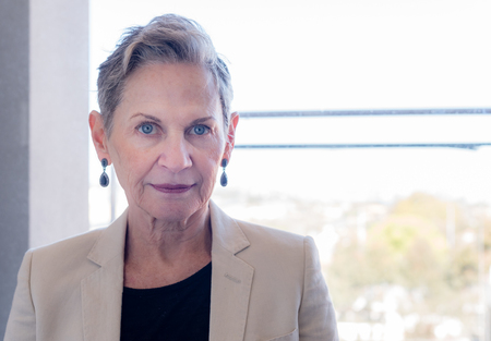 Head and shoulders view of beautiful older woman with short grey hair and beige jacket against...