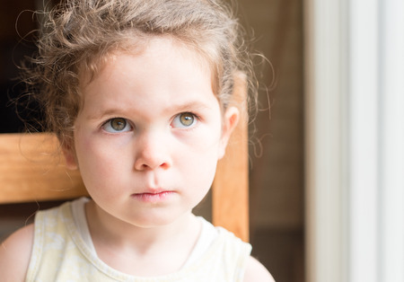Portrait of little girl sitting next to window looking sad (selective focus)の写真素材