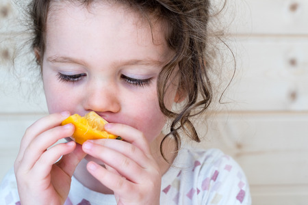 Close up of little girl eating orange piece (selective focus)の写真素材