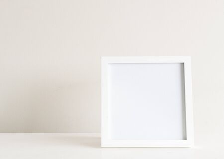 Square white blank picture frame on shelf against neutral wall background