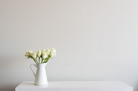 White roses in small jug on shelf against neutral wall backgroundの写真素材