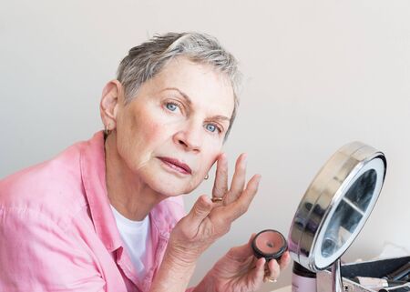 Cropped view of beautiful older woman with short grey hair applying makeup (selective focus)の写真素材