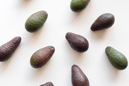 High angle view of organic green and black Hass avocados arranged on white table background