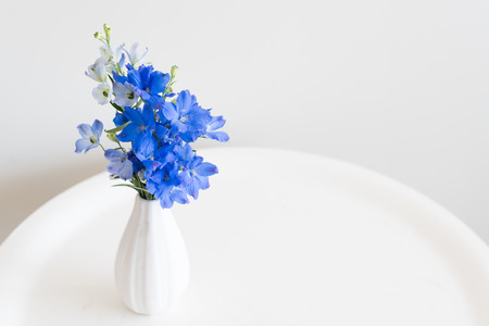 High angle close up view of blue delphinium flowers in small white vase on round table (selective focus)の写真素材