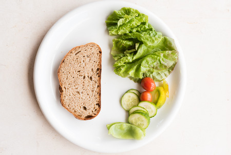 High angle view of white plate with brown bread and healthy salad including lettuce, tomato and...