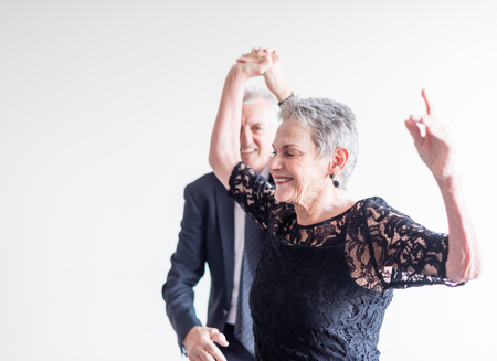 Close up of elegantly dressed older man and woman dancing exuberantly against neutral background (selective focus)の写真素材