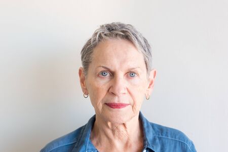 Portrait of beautiful older woman with short grey hair and striking blue eyes against neutral background (selective focus)の写真素材