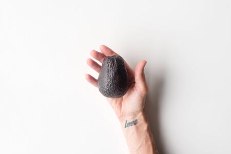 High angle view of woman's hand with love tattoo holding ripe avocado on white backgroundの写真素材