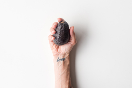 High angle view of woman's hand  with love tattoo holding ripe avocado on white backgroundの写真素材