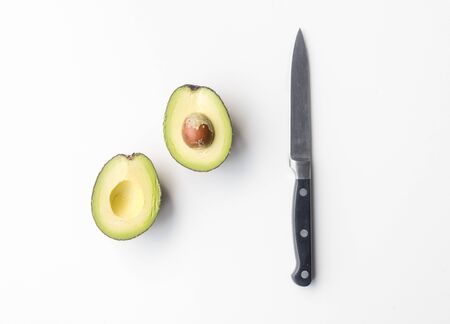 Directly above view of avocado cut in half with knife on white tableの写真素材