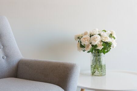 Cropped close up view of retro armchair and roses in glass jar on small white table (selective focus)の写真素材