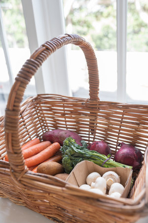 Closeup vertical view of wicker basket with vegetables from farmers market including mushrooms,...