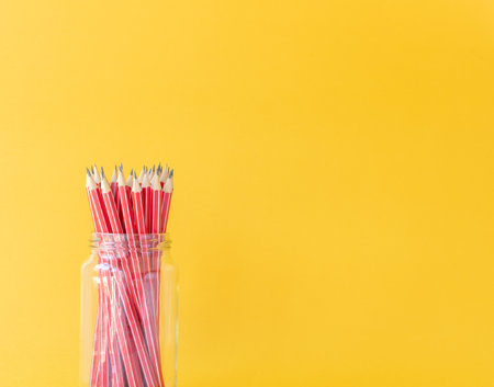 Closeup of red HB pencils in glass jar against yellow background with copy space - back to school conceptの写真素材