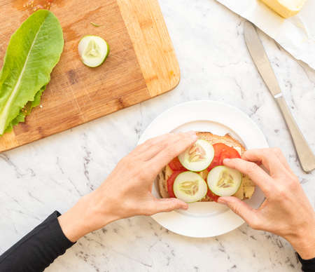 High angle view of hands adding cucumber  to salad sandwich  against grey marble backgroundの写真素材