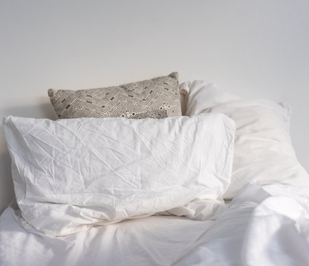 Closeup of rumpled pillows and cushions on white bed (selective focus)