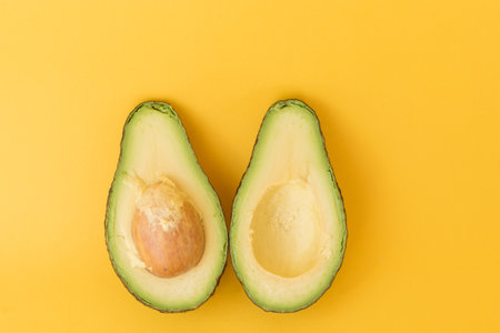 High angle view of avocado cut in half on yellow background (selective focus)
