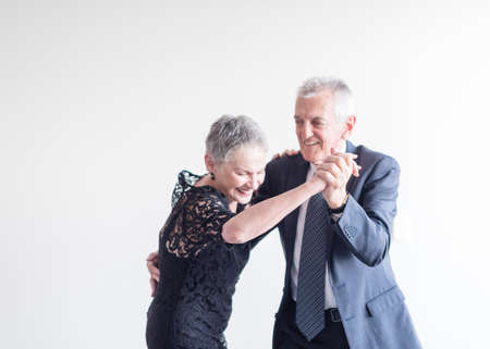 Waist up view of elegantly dressed older man and woman dancing with focus on clasped hands against neutral background (selective focus)の写真素材