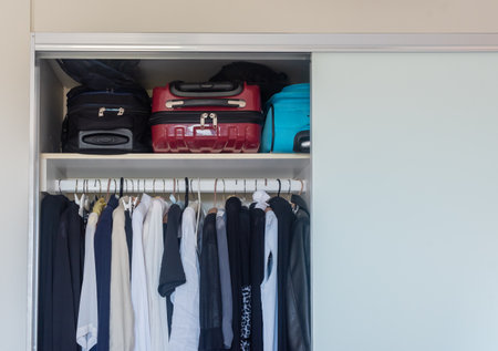 Cropped view of women's black and white clothing hanging neatly in wardrobe with suitcases above (selective focus)の写真素材