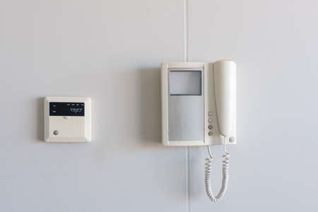 Close up of telephone-style video intercom and airconditioning thermostat on apartment wall