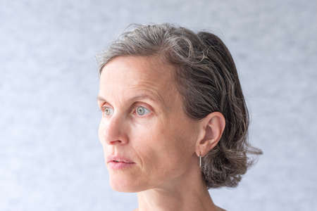 Close up side view of natural looking middle aged woman with grey hair and green eyes (selective focus)の写真素材