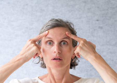 Middle aged woman with grey hair holding up wrinkles above eyes (selective focus)
