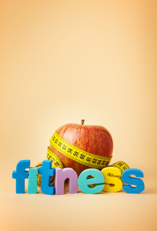 Red apple with yellow measuring tape. Colored letters "FITNESS".の写真素材