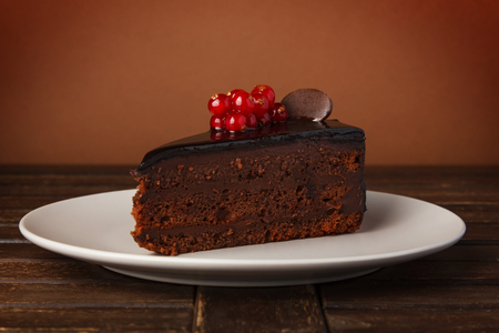 Chocolate cake plate. Decoration of fresh red currant berries, mint and chocolate pieces. Cake on a plate on a wooden table.の写真素材