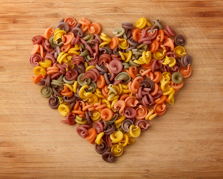 Heart of colored pasta on a wooden background. Homemade food.の写真素材