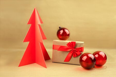 Gift box with bow and red balls with woodden Christmas tree on a natural brown background.の写真素材