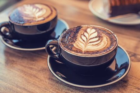 Two black cups of coffee with art on a table, blurred desert on the backgroundの写真素材