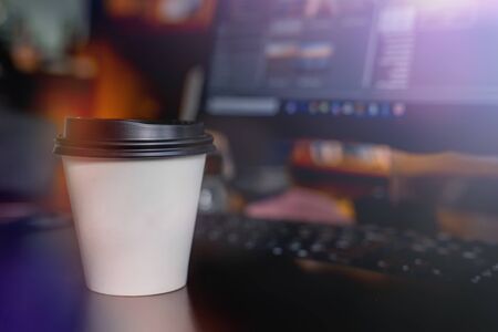 A cup of coffee takeaway on the desk with a monitor on backgroundの写真素材