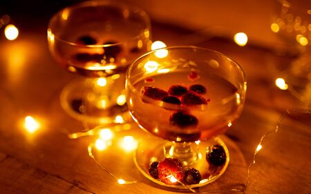 Two cocktail glasses with berries and lights glowing on wooden background still lifeの写真素材
