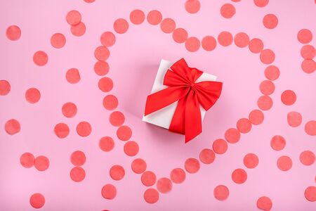 Gift box with red bow and confetti in shape of heart aroundの写真素材