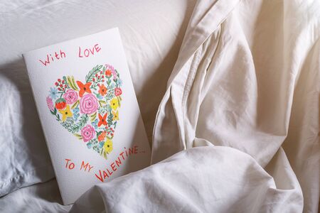Valentines day handmade painted card in watercolor in a bed on the pillow. Showing love and giving the present for the partnerの写真素材