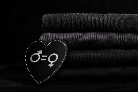 Black clothes in pile and wooden board in the shape of heart with written symbols of sex and equal sign. Gender equality concept.の写真素材