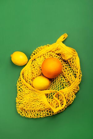 Fruit lemons and orange in yellow string mesh reusable bag on the green background, zero waste eco concept.の写真素材