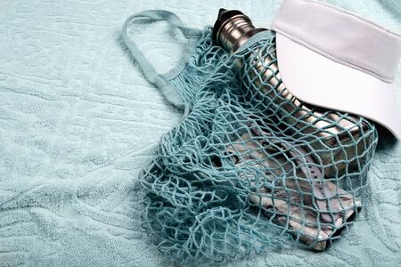 Bottle of water, mobile phone and smart watch in blue string mesh reusable bag and white visor on...