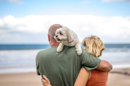 Man and woman hugging and holding a small cute white dog on a shoulderの写真素材
