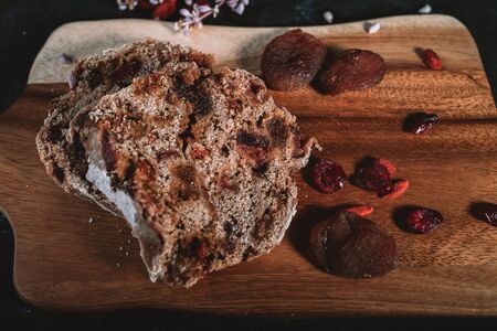 Homemade fruit bread on wooden chopping board with scattered dry berries and flowers on background...