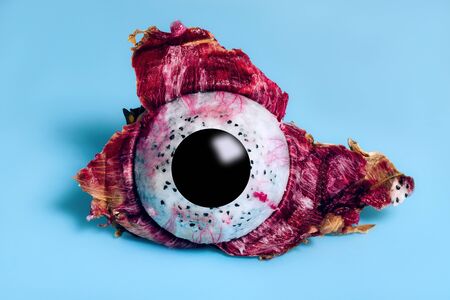 Dragon Fruit or Pitaya half peeled from the skin with black circle depicting eye pupil on blue...