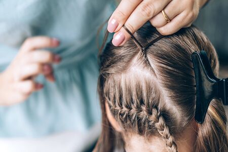 Mother does hair braid to her daughter, close up photo.