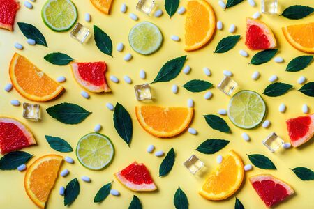 Pattern of citrus lemon, lime, orange and grapefruit slices, mint herbs, cubes of ice and fresh pills on yellow background. Top view. Minimal design background.の写真素材