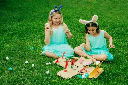 Cute little children wearing bunny ears on Easter day sitting on grass in garden and playing with...