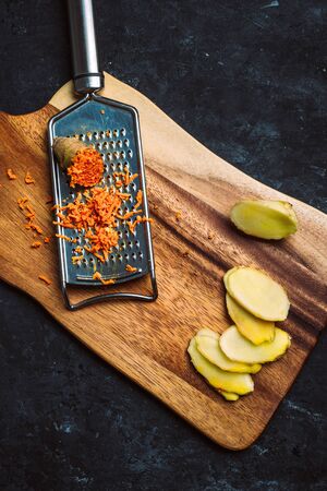 Ginger and turmeric roots with hand grater on wooden chopping board on black background.の写真素材