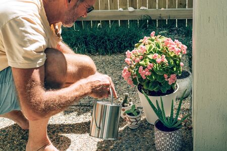 A man plants and watering plants in a backyard.