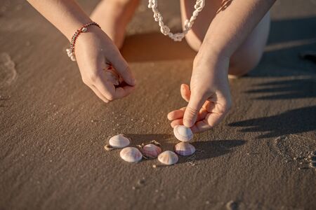 Little girls hands creating a heart from seashells on the ocean sandy beach. Summer leisure, love concept.の写真素材