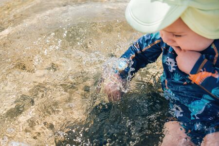Baby boy sitting in the sea water and splashing it by hand,の写真素材