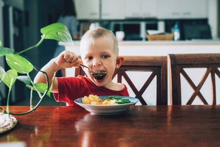 Cute child, preschool boy, eating veggies for lunch in the dining room.の写真素材