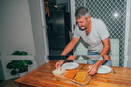 Man serving dinner from the delivered Indian food from a restaurant. Plastic containers with delicious food on the table.の写真素材