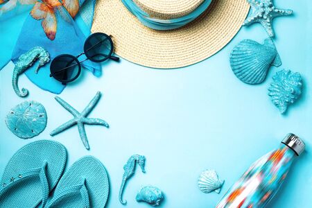Summer fashion on blue and coral background. Blue flip flops, seashells, sunglasses, bottle and straw hat. Flat lay, top view with copy space.の写真素材